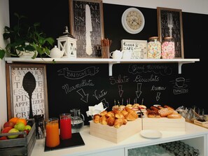 Ein Frühstücksbuffet mit verschiedenen Backwaren, einer Kreidetafel mit Speisekarte und einer Uhr an der Wand.