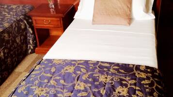 A hotel room with a bed, a nightstand, a vase with flowers, and a patterned bedspread.
