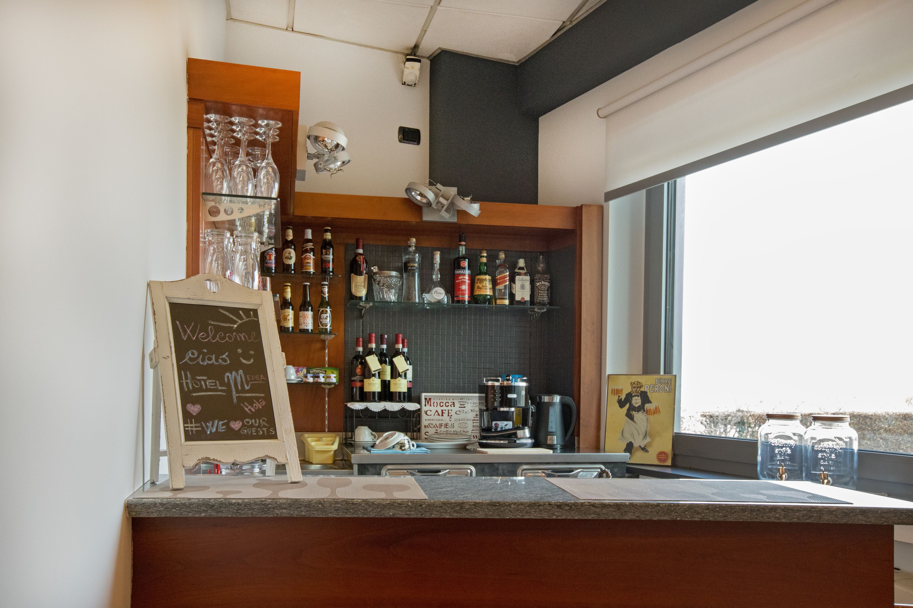 Uma área de bar com um quadro-negro, prateleiras com garrafas e uma máquina de café.