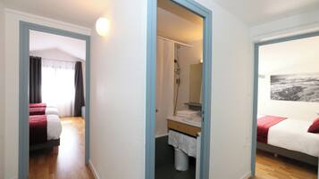 Habitación de hotel con piso de madera, una cama con cubrecama rojo y blanco, baño con ducha y un ventanal con vistas.