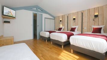 Een hotelkamer met drie bedden, houten vloeren, een televisie aan de muur en een accentmuur van hout.
