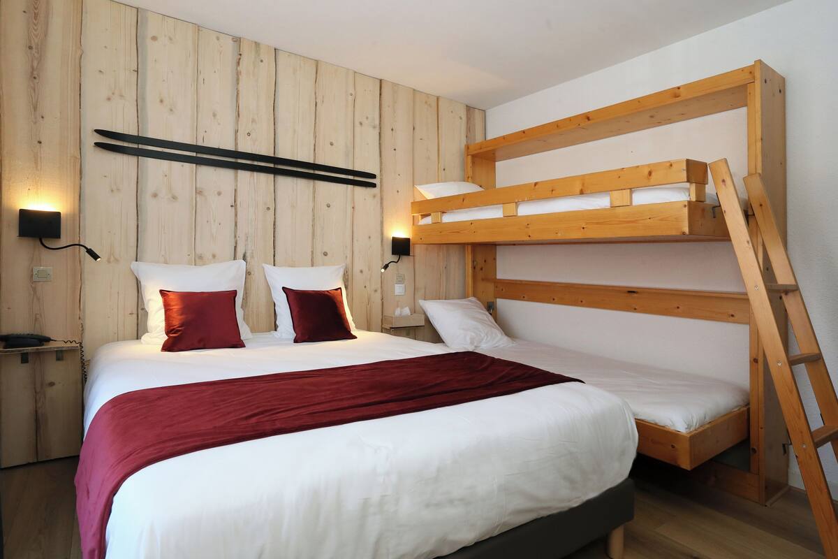 A bedroom with a bunk bed, wooden walls, a bedside table, and a red throw blanket.
