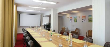A conference room with a long table, chairs, a projector screen, and a whiteboard.