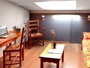 A room with a wooden desk, a chair, a small table with a vase, and a bed with a floral bedspread.