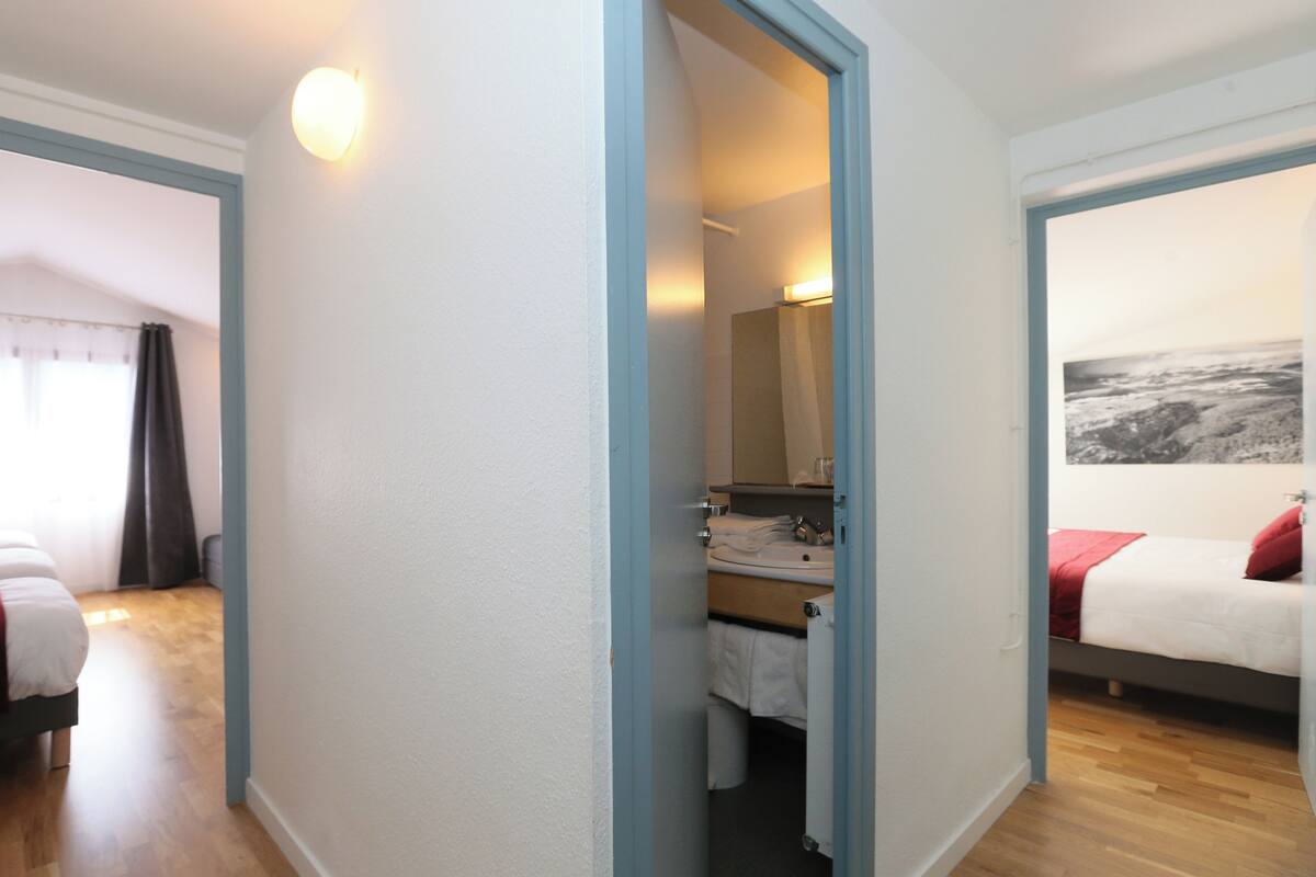 A hotel room with two beds, a bathroom with a mirror, and a view of the sea.