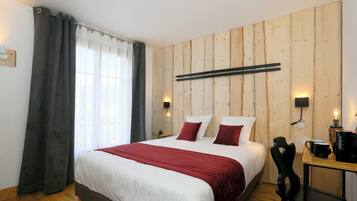 Ein Hotelzimmer mit einer Holzpaneelausstattung, einem Bett mit weißer und roter Bettwäsche, einem schwarzen Sessel, einem kleinen Tisch mit einer Kaffeemaschine und einem Fenster mit Vorhängen.