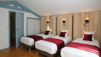 A room with three beds, wooden panel walls, and wall-mounted lights.