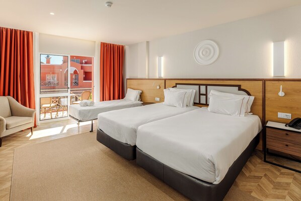 Une chambre d’hôtel avec deux lits, un canapé, une petite table et un balcon avec des rideaux orange.