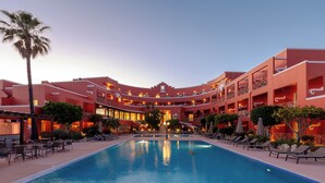 Un hotel con piscina central, varios balcones y fachada roja.