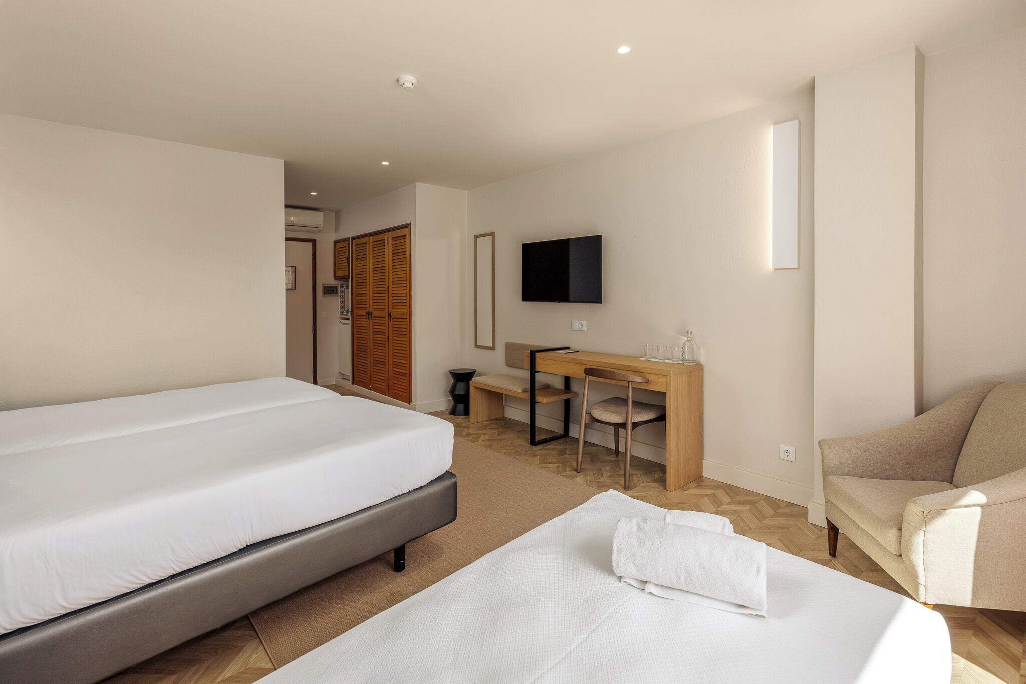 Una camera d'albergo con due letti, una scrivania, una sedia, una televisione e un divano.