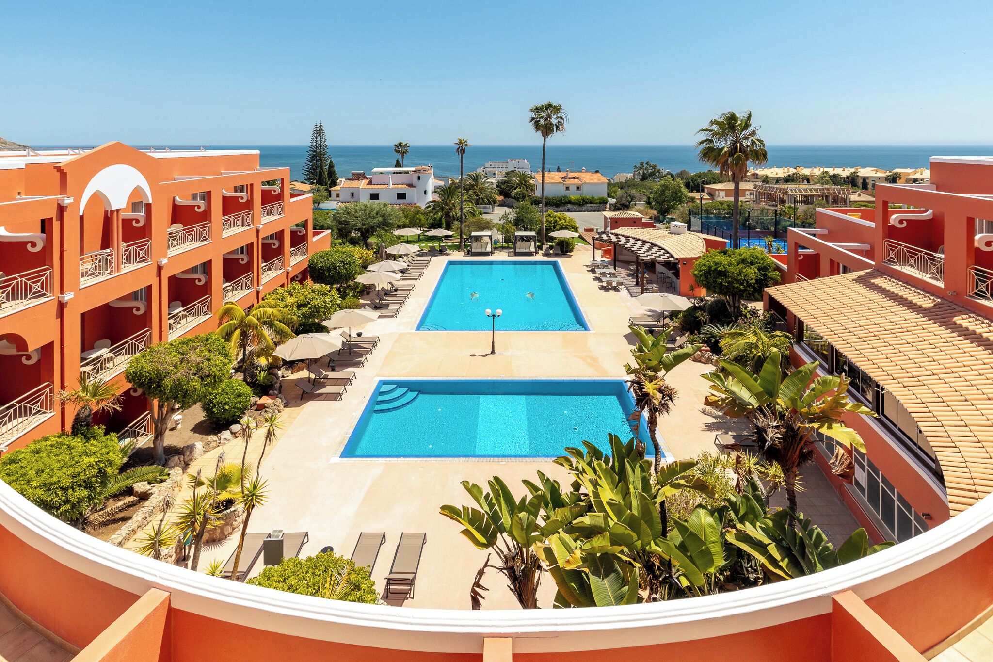 A resort with a central swimming pool, multiple balconies, and a view of the ocean.