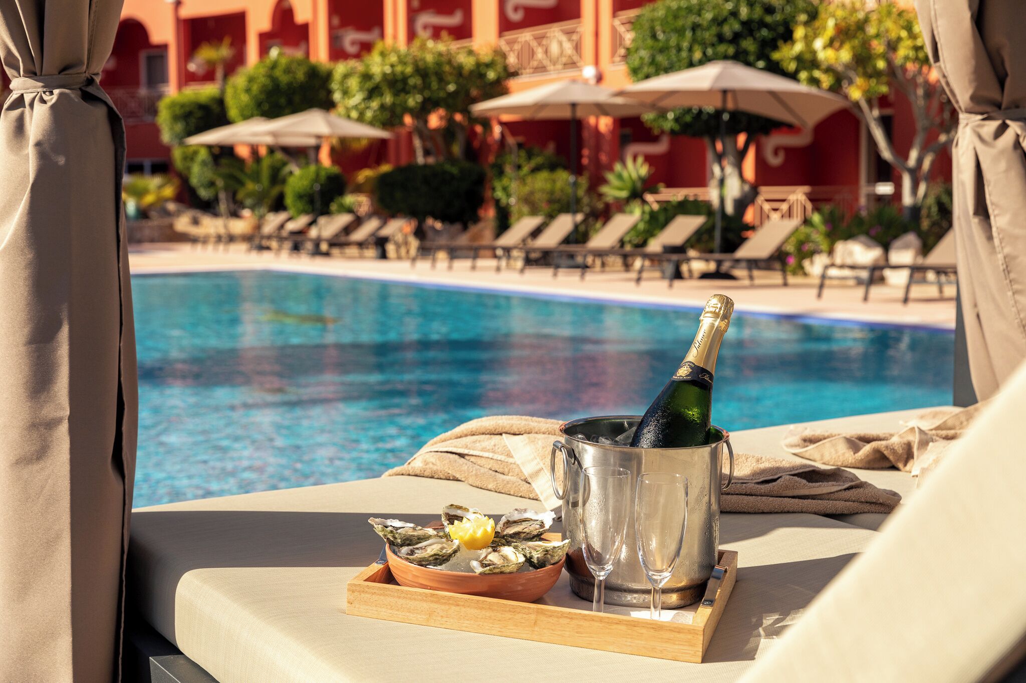 A poolside view with a champagne bottle, a bowl of oysters, and a glass of champagne on a tray.