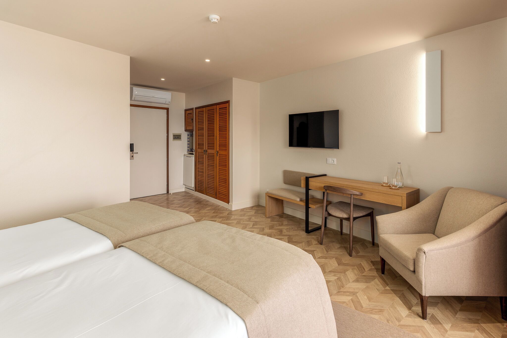Ein Hotelzimmer mit zwei Betten, einem Schreibtisch, einem Sessel, einem Fernseher und einem Holzschrank.