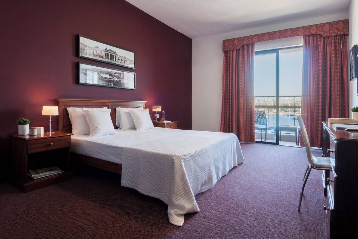 A hotel room with a bed, nightstands, a desk, and a view of a balcony.