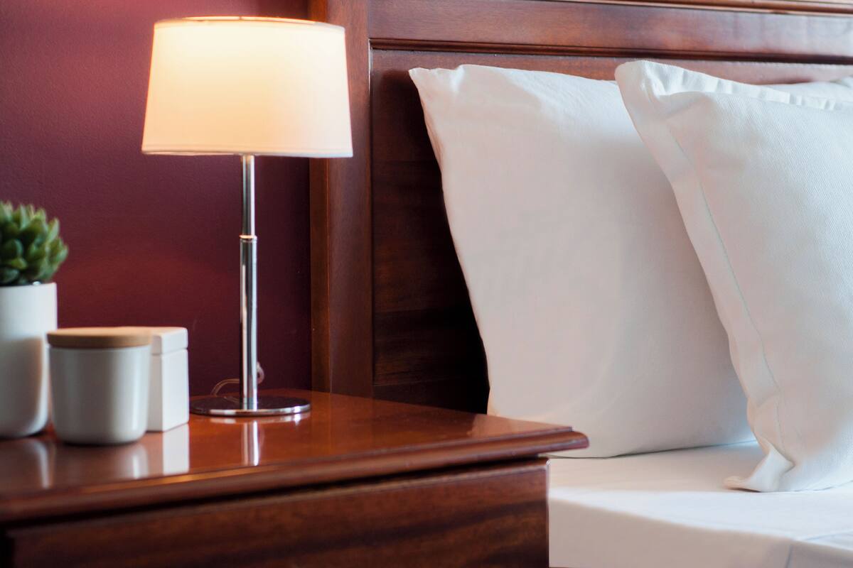 A wooden bedside table with a lamp, a white pillow, and a small potted plant.