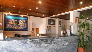 Zona de recepción de hotel con mostrador de mármol, techo de madera y varias obras de arte enmarcadas.