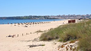 Una playa con sombrillas, una orilla arenosa y un paisaje urbano al fondo.