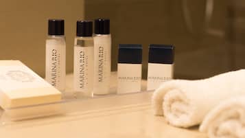 A bathroom with toiletries including bottles of Marinaric Hotel products and a rolled white towel on the counter.