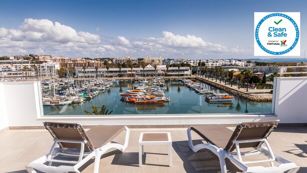 A terrace with two white lounge chairs and a small table, overlooking a marina with boats and a clear sky. - Marina Rio (Lagos)