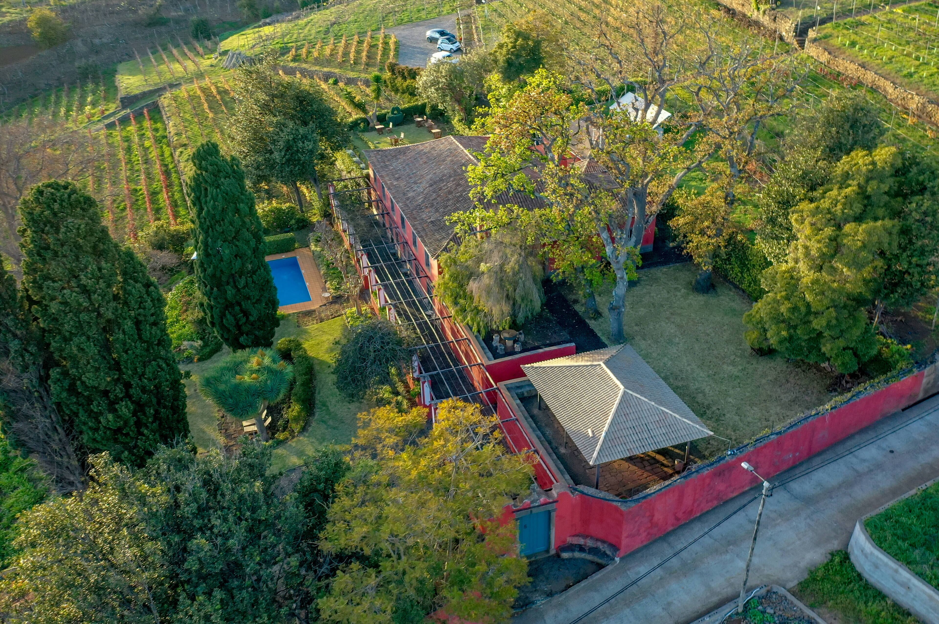 An aerial view of a property with a red building, a swimming pool, and surrounding green fields.