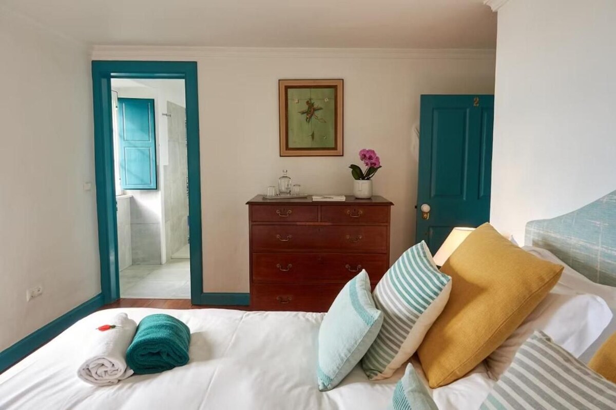 Un dormitorio con cama, almohadas, cómoda, espejo y puerta.