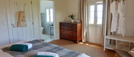 Een slaapkamer met een bed, twee opgerolde handdoeken, een houten dressoir, een bankje en een kledingrek.