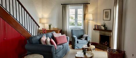 A living room with a red wall, a blue sofa, a grey armchair, a wooden coffee table, and a fireplace.