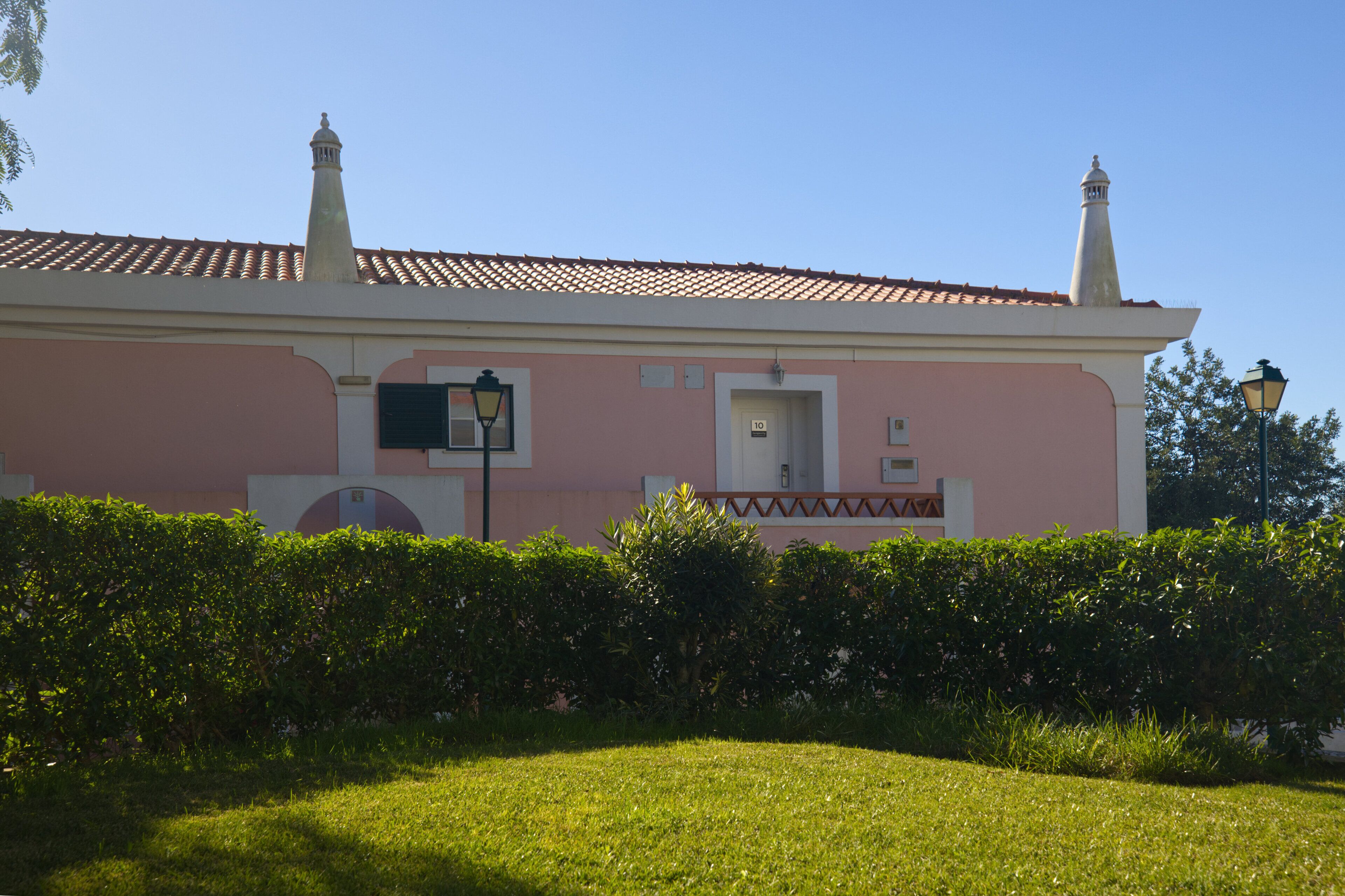 A pink building with a tiled roof, a door, and a small balcony.