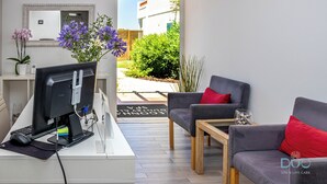 A modern living room with a computer setup, two grey sofas with red cushions, a small wooden table, and a potted plant. - Cegonha Country Club (Loulé)