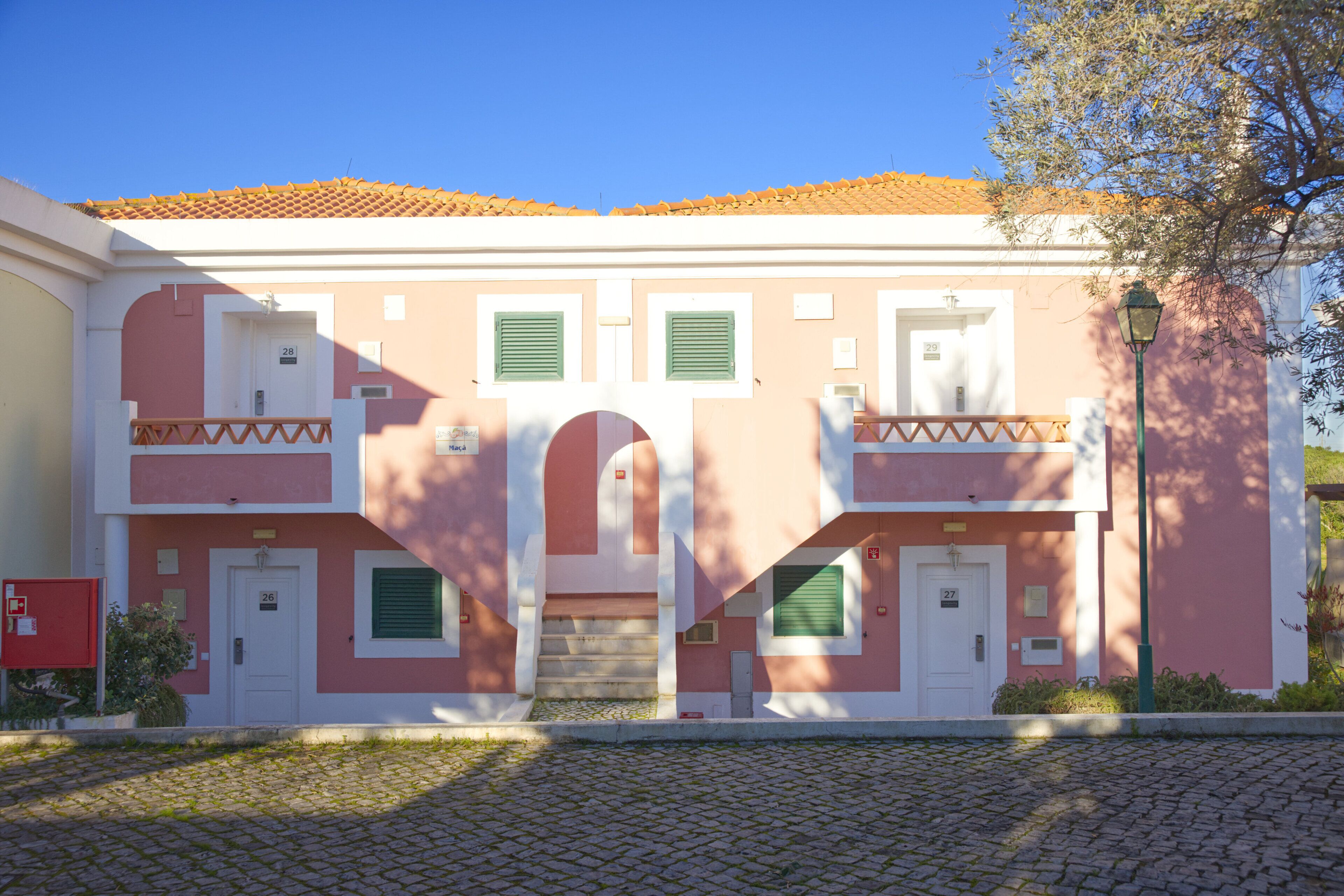 A two-story building with a pink facade, green shutters, and a tiled roof.