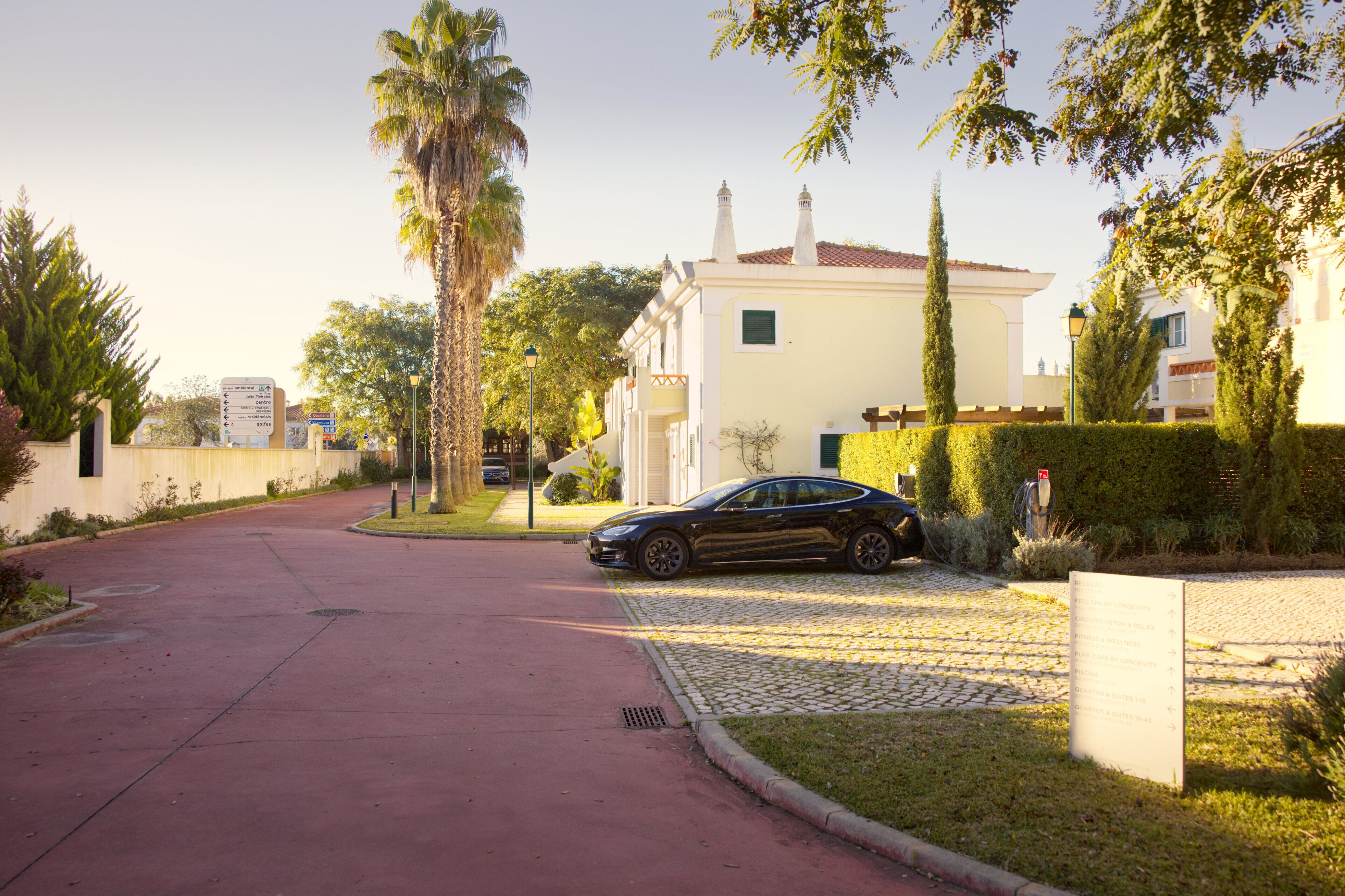A residential street with a parked car, a house with a tiled roof, and a signboard.