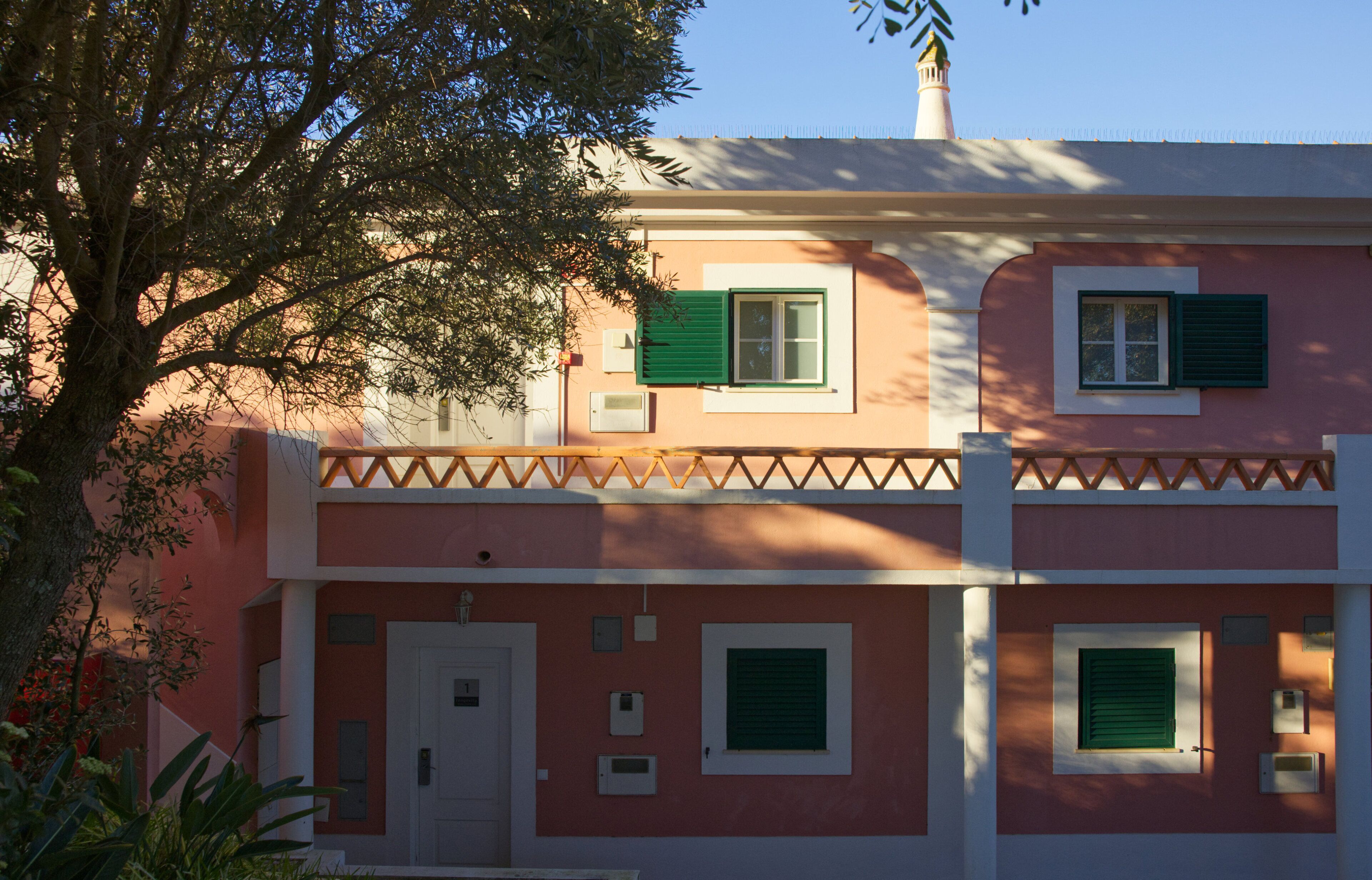 Un immeuble de deux étages avec une façade rose, des volets verts et une porte blanche.