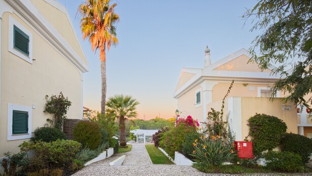 A cobblestone pathway leading to a building with a white facade and green shutters. - Cegonha Country Club (Loulé)