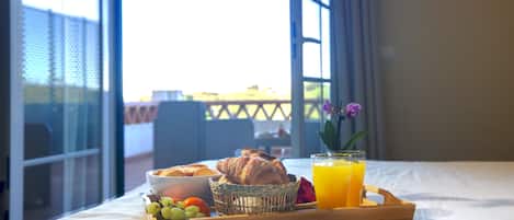 A breakfast tray with croissants, grapes, strawberries, and orange juice on a bed with a view of a balcony.