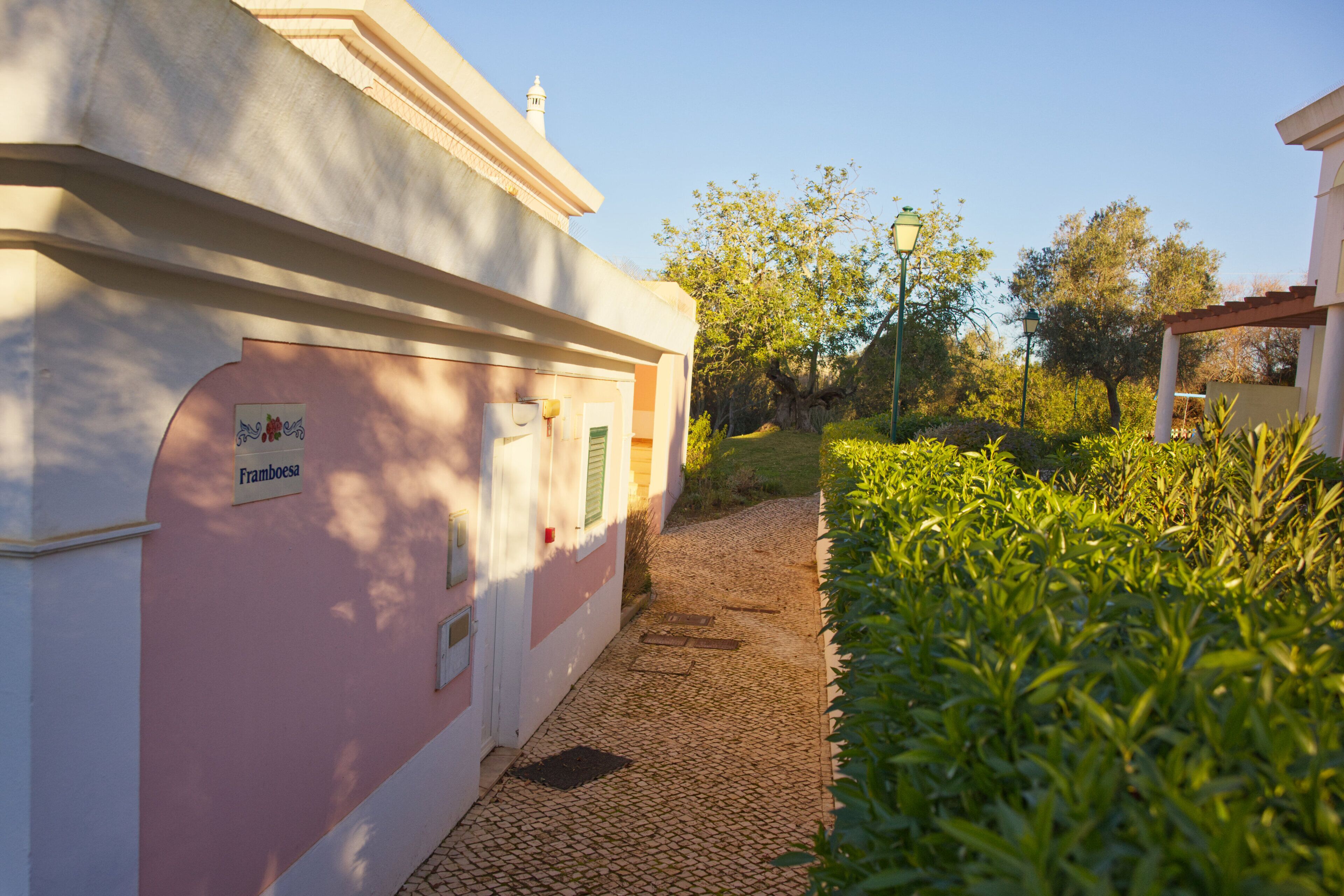 A narrow cobblestone path leading to a building with a pink facade and a sign reading "Framboesa."