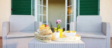 A wicker table set with breakfast items, two wicker chairs, and a view of a green door.