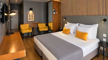 Una habitación de hotel con cama, mesitas de noche, un escritorio con silla, una pequeña mesa con sillas y un televisor instalado en la pared.