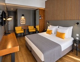 Una habitación de hotel con cama, mesitas de noche, un escritorio con silla, una pequeña mesa con sillas y un televisor instalado en la pared.