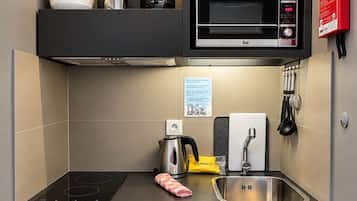 Cozinha compacta com micro-ondas, chaleira, pia e prateleiras de armazenamento.
