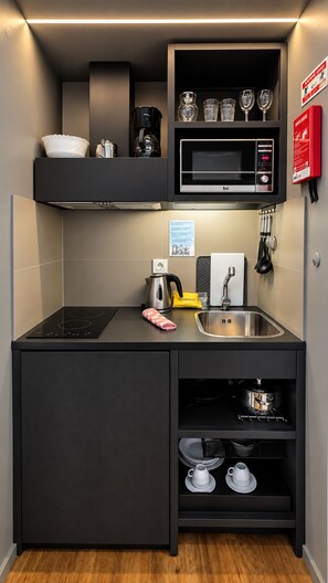 Cocina compacta con microondas, hervidor, pileta y estantes de almacenamiento.