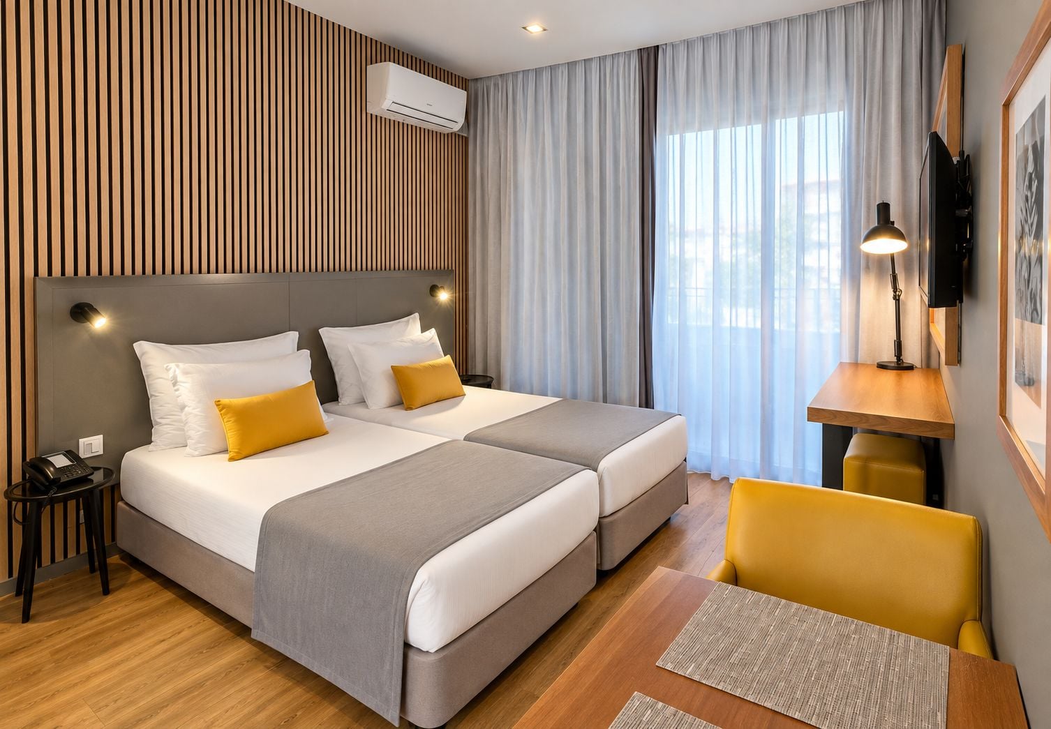 A hotel room with two beds, a desk, a chair, a phone, an air conditioner, and a TV.