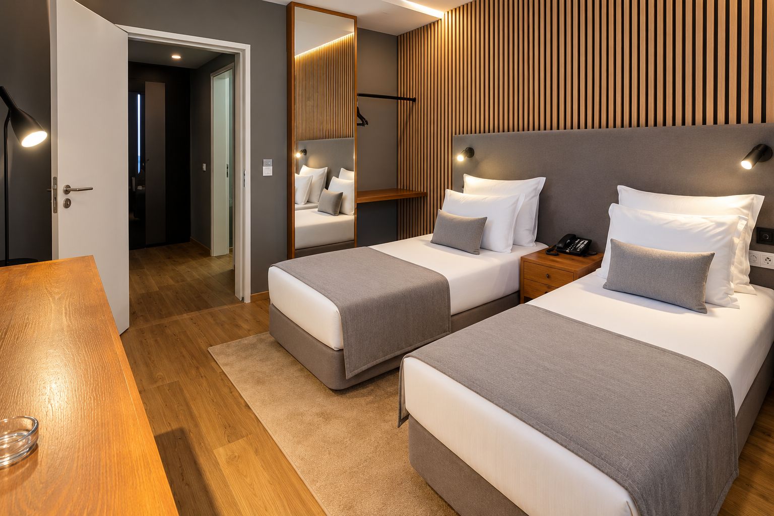Habitación de hotel con dos camas, una mesa de madera, un espejo y una mesita de noche con un teléfono.