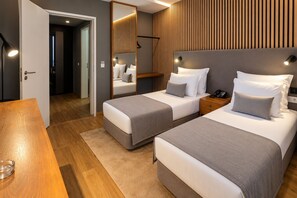 A hotel room with two beds, a wooden table, a mirror, and a nightstand with a phone. - Paraíso - Touristic Apartments (Funchal)