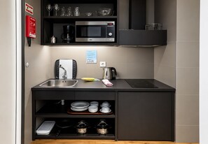 Una cocina compacta equipada con microondas, lavamanos y hervidor.