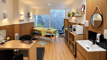 Uma sala de spa moderna com uma mesa de massagem, uma pequena escrivaninha com uma cadeira, uma pia e um espelho.