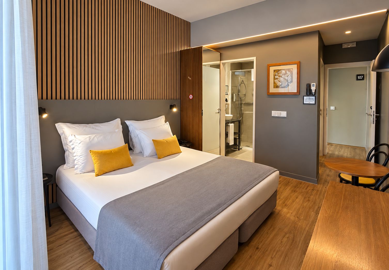 A hotel room with a bed, bedside table, and a small seating area.