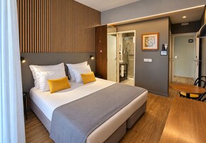 Habitación de hotel con cama, mesita de noche y un pequeño rincón de descanso.