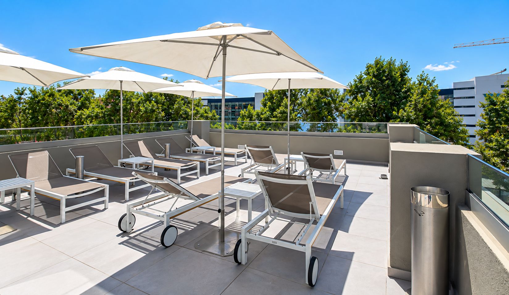 Une terrasse sur le toit, dotée de chaises longues, de parasols et offrant une vue sur le paysage urbain.