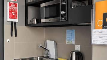 Cocina compacta con lavabo, estufa y microondas. Hay repisas con vajilla y una tetera.