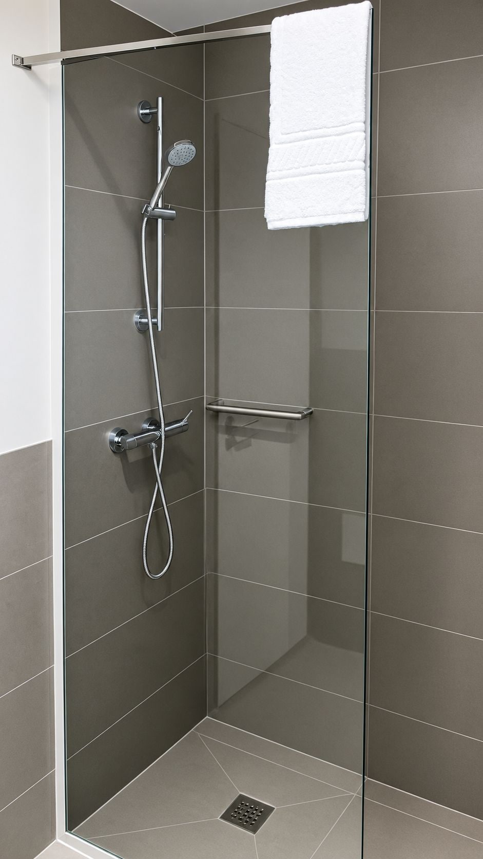 Cabina de ducha con paredes de vidrio, ducha de mano, grifo empotrado en la pared y una toalla colgada en la puerta.